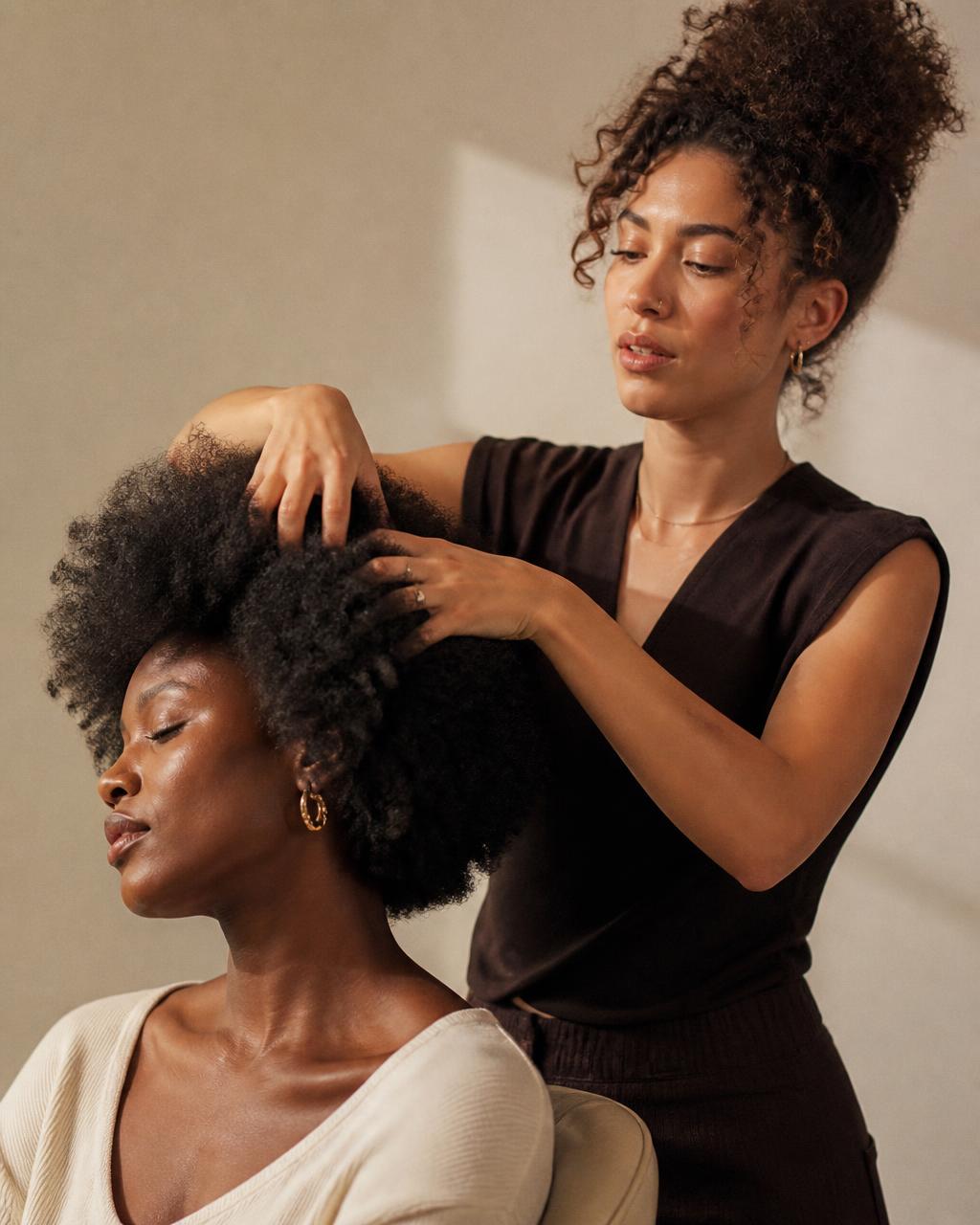 A hairstylist shaping a client's textured curls with her fingers, the finished silhouette catching warm studio light.